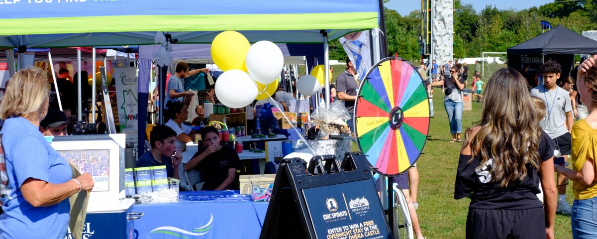 Idea Stream Marketing team booth at Commack Day 2025, featuring the prize wheel, community visitors, and local vendors.