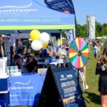 Idea Stream Marketing team booth at Commack Day 2025, featuring the prize wheel, community visitors, and local vendors.