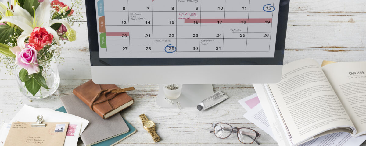 Desktop with a laptop showing a content calendar, notebook, pen, and coffee cup in a clean workspace.