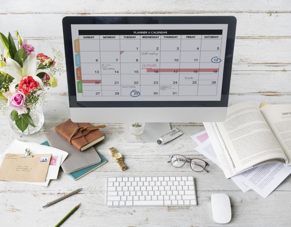 Desktop with a laptop showing a content calendar, notebook, pen, and coffee cup in a clean workspace.