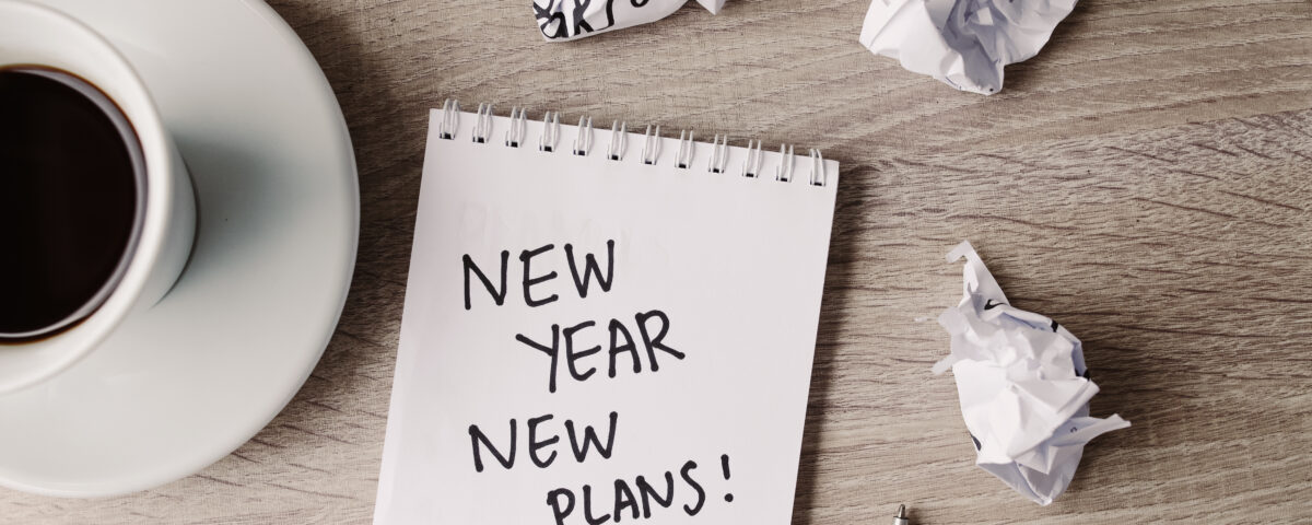Desk with a notepad that says “New Year, New Plans” and office supplies, symbolizing marketing planning.