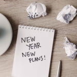 Desk with a notepad that says “New Year, New Plans” and office supplies, symbolizing marketing planning.