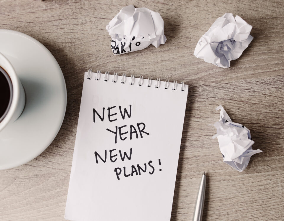 Desk with a notepad that says “New Year, New Plans” and office supplies, symbolizing marketing planning.