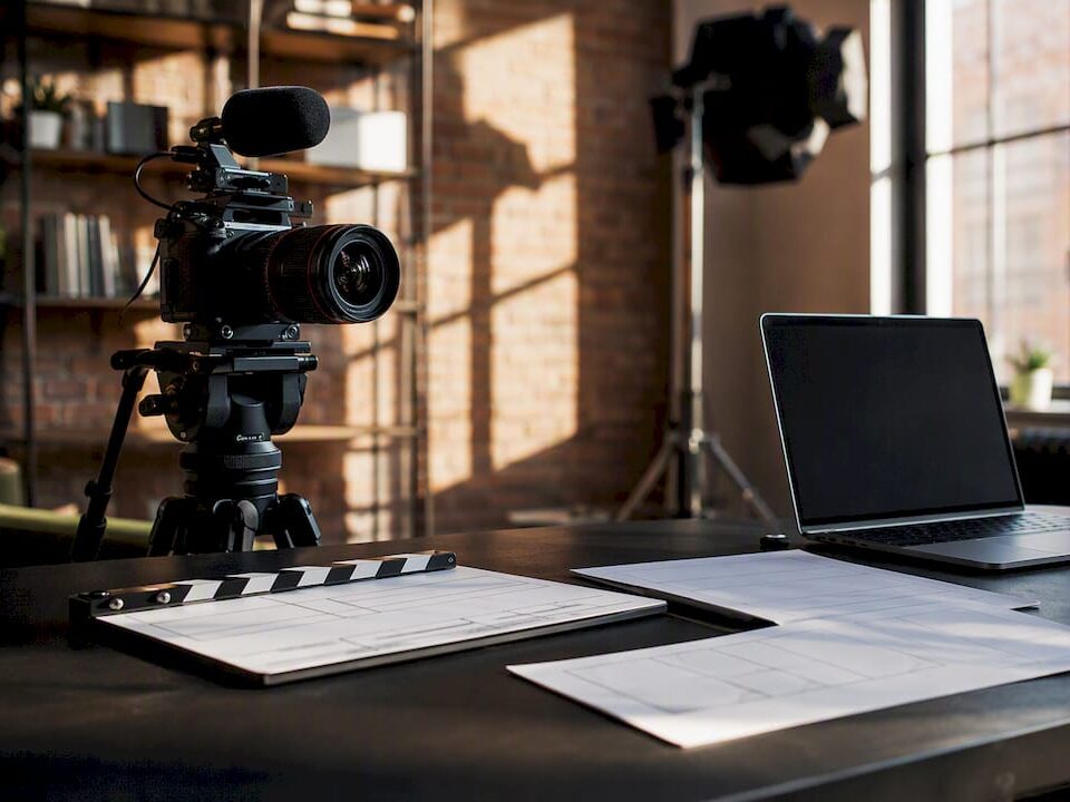 Video production setup with a camera, laptop, and clapperboard on a table.