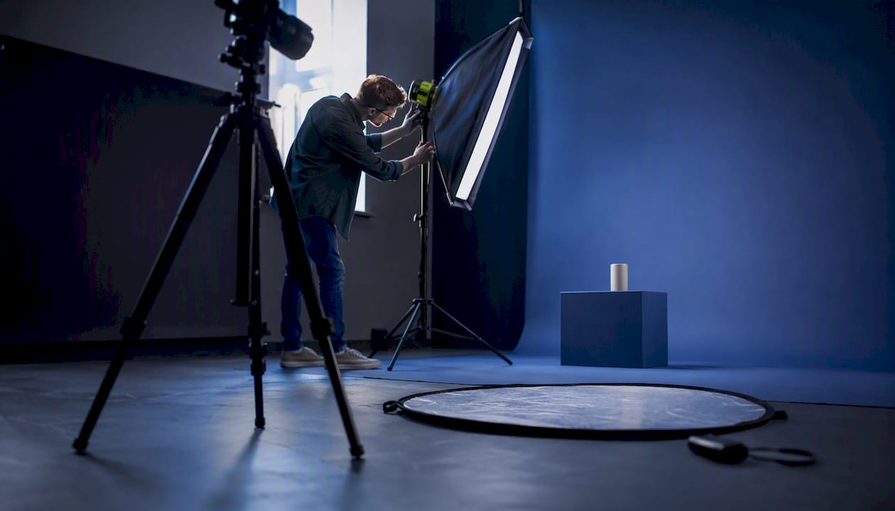 Photographer adjusting lighting in a blue photography studio with a circular reflector on the floor.